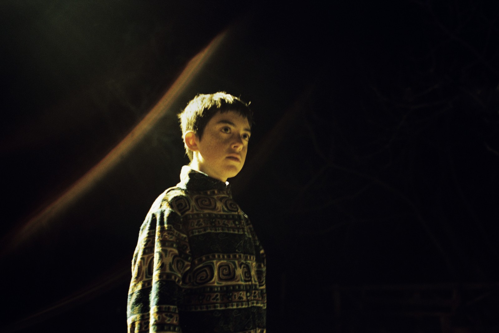Ein Junge steht draußen in der Dunkelheit.